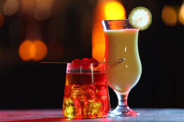 Glasses of alcoholic cocktails with garnish on table against blurred background, bokeh effect