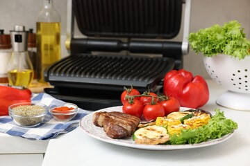 Electric grill, tasty meat, vegetables, mushrooms and spices on white table in kitchen, closeup