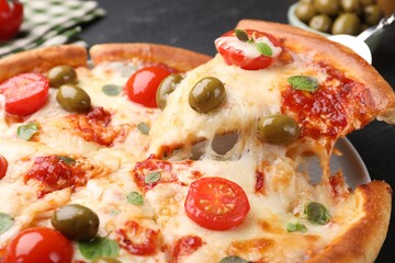 Taking piece of delicious pizza with cheese, tomatoes and olives at table, closeup