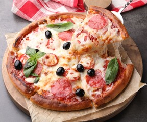 Taking piece of delicious pizza with cheese, salami, olives and basil at grey table, closeup