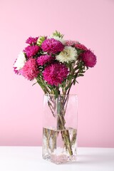 Beautiful flowers in vase on white wooden table against pink background