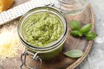 Fresh pesto sauce in jar, grater and ingredients on grey textured table, closeup