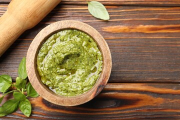 Fototapeta na wymiar Fresh pesto sauce in mortar, pestle and basil leaves on wooden table, flat lay. Space for text