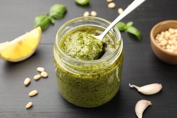 Taking fresh pesto sauce with spoon from jar at black wooden table, closeup