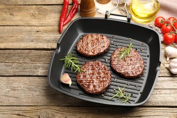Pan with grilled patties, tomatoes and spices on wooden table, closeup. Space for text