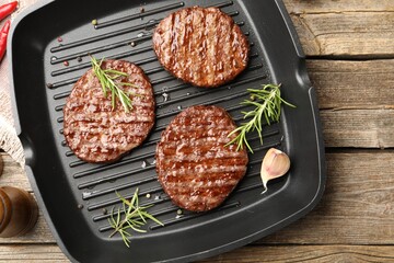 Pan with grilled patties and spices on wooden table, top view