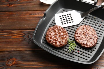 Pan with grilled patties, spices and slotted spatula on wooden table, above view. Space for text