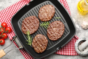 Pan with grilled patties, tomatoes and spices on grey table, flat lay