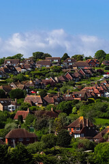 Houses and lush green trees cover a sunny suburban hillside under a blue sky. East Sussex...