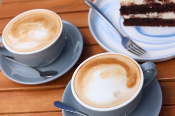 Cups of aromatic coffee and slice of cake on wooden table, closeup