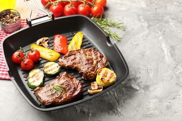 Pan with grilled beef steaks, mushrooms, vegetables and spices on grey textured table, closeup. Space for text