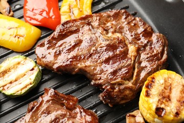 Grilled beef steaks and vegetables on black pan, closeup