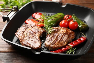 Pan with grilled beef steaks, rosemary and vegetables on wooden table, closeup