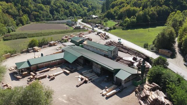 Aerial view of a sawmill factory in the mountains surrounded by dense forest, with stacks of processed lumber and timber. Wood industry and natural resource production	