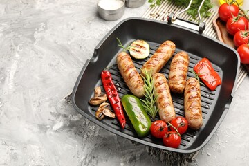 Pan with grilled sausages, vegetables, mushrooms and spices on gray textured table, closeup