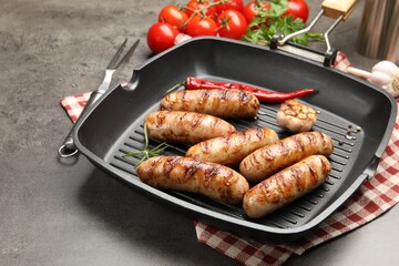 Pan with grilled sausages, spices and tomatoes on gray textured table, closeup