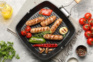 Pan with grilled sausages, vegetables, mushrooms and spices on gray textured table, flat lay