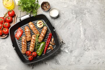 Pan with grilled sausages, vegetables, mushrooms and spices on gray textured table, flat lay. Space for text