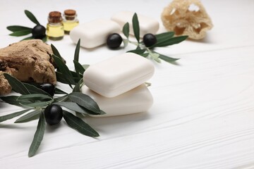 Handmade soap bars, olives, snag, green leaves, essential oils and loofah on white wooden table, closeup. Space for text