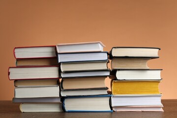 Stacks of many books on wooden table against light brown background