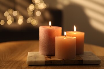 Burning candles on wooden table against blurred lights indoors, closeup. Space for text