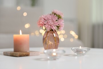 Burning candles and beautiful flowers on white table indoors, closeup. Bokeh effect