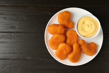 Tasty chicken nuggets with sauce on black wooden table, top view. Space for text
