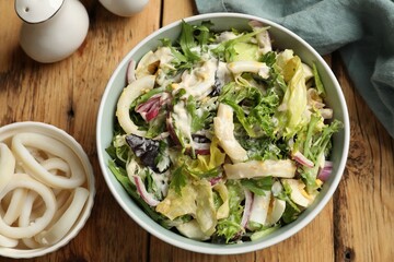 Tasty salad with squid rings, onion and eggs served on wooden table, flat lay