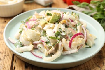 Tasty salad with squid rings, onion and eggs served on wooden table, closeup
