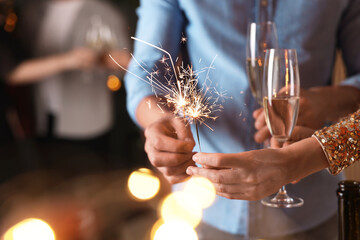 Friends celebrating New Year with sparklers and wine glasses indoors, closeup