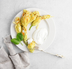 fried zucchini flowers, cooked zucchini or pumpkin blossoms on white plate with yogurt with gray napkin, top view, copy space