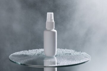 Close-up view of a small white spray bottle on a misty glass surface