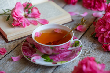 A cup of aromatic tea, a book and a rose on the table.
