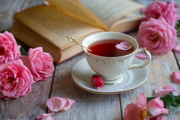 A cup of aromatic tea, a book and a rose on the table.