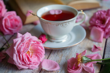 A cup of aromatic tea, a book and a rose on the table.