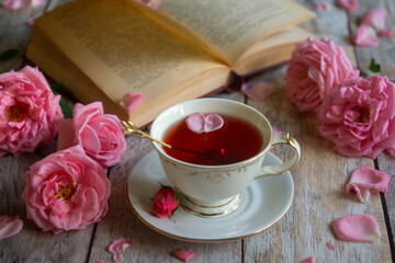 A cup of aromatic tea, a book and a rose on the table.