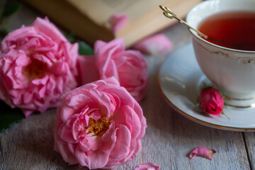 A cup of aromatic tea, a book and a rose on the table.