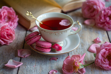 A cup of aromatic tea, a book and a rose on the table.