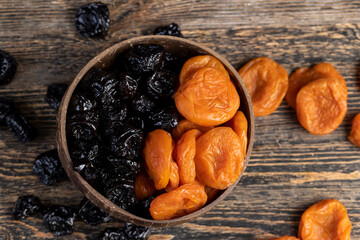 dried apricots and black prunes made from ripe blue plums mixed together in a plate , dried plums and apricots in a bowl made from natural materials
