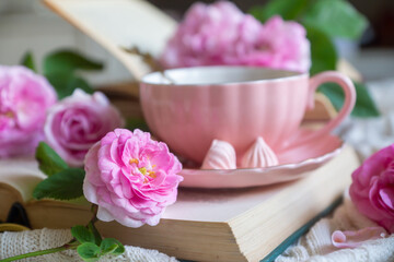 A cup of aromatic tea, a book and a rose on the table.
