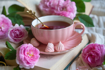 A cup of aromatic tea, a book and a rose on the table.
