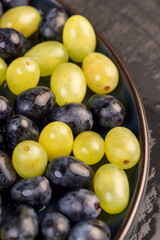 wet beautiful ripe grapes of blue and green color lying on a bowl, covered with drops of water, wet fruits of pure green and blue grapes during cooking