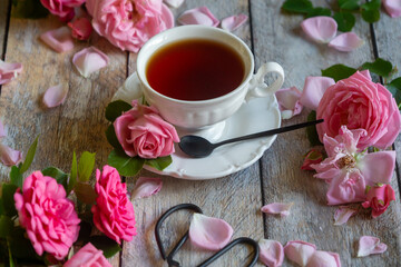 A cup of aromatic tea, a book and a rose on the table.