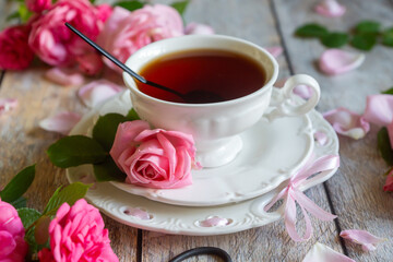 A cup of aromatic tea, a book and a rose on the table.