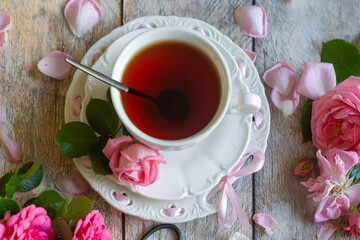 A cup of aromatic tea, a book and a rose on the table.