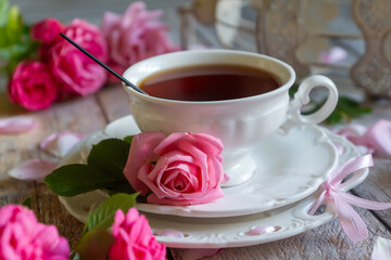 A cup of aromatic tea, a book and a rose on the table.