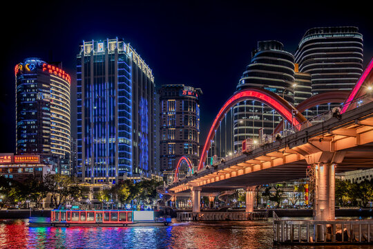 Guangzhou, Canton, China, 1 March 2025. Haizhu Bridge with illuminated arches and neon skyline at night, with a tourist boat reflecting colorful lights in the Pearl River.