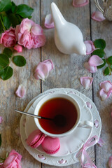 A cup of aromatic tea, a book and a rose on the table.