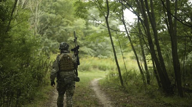 Camouflaged and masked army soldier with AR15 carbine with a collimator on a mission. Carefully scouting a green forest
