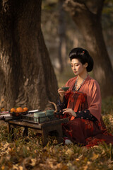 Woman in traditional dress enjoying tea outdoors in a serene setting.